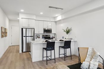 A modern kitchen with a white island and black chairs.